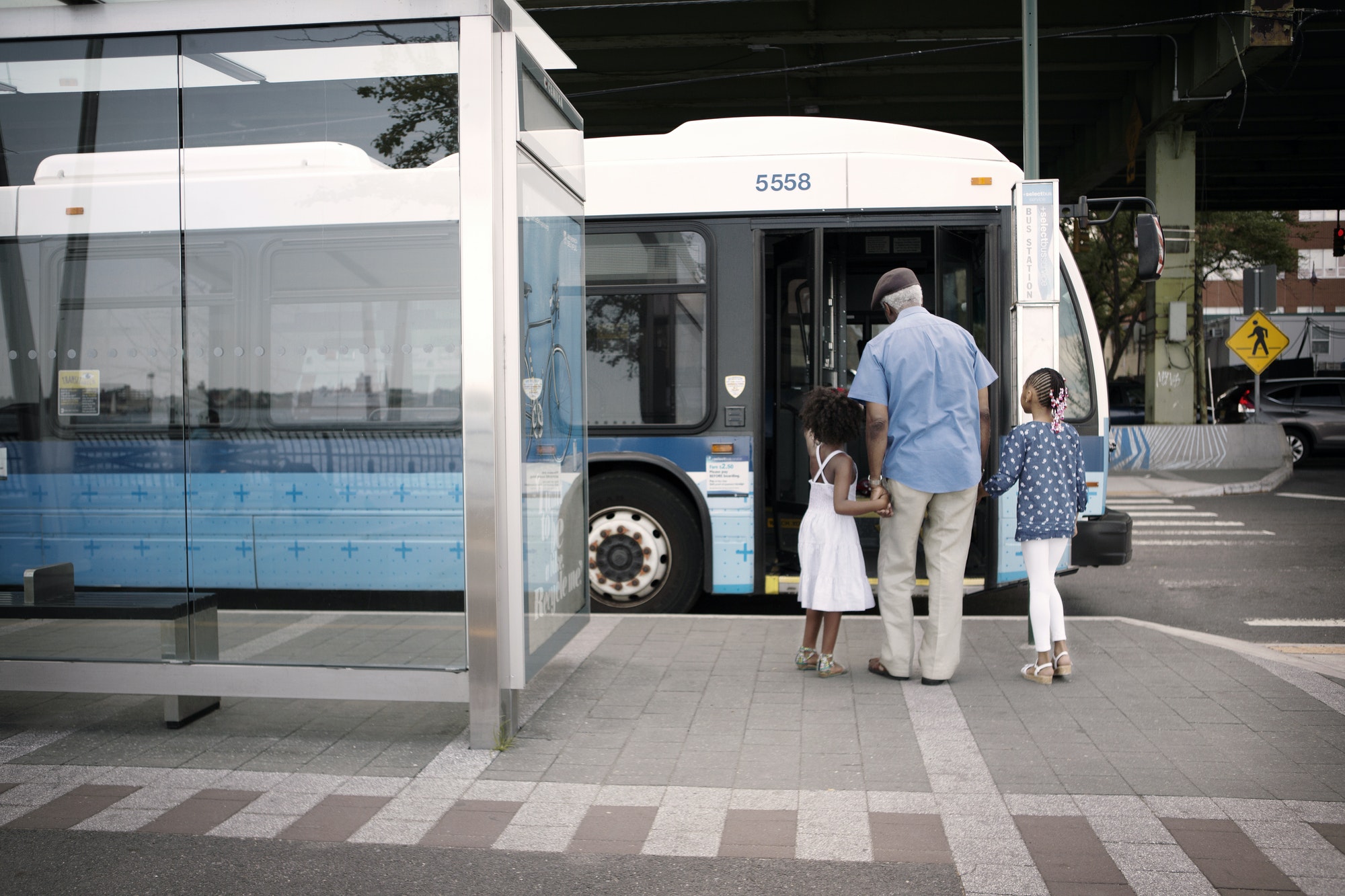 Rear View Of Grandfather And Grandchildren Walking Towards Bus At City
