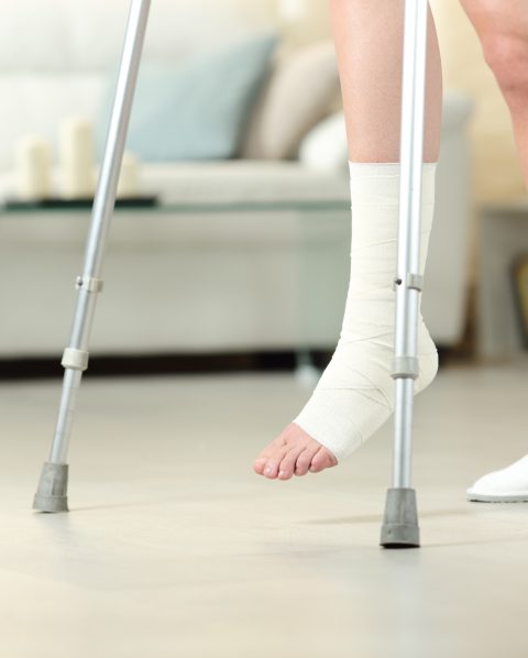 Side view portrait of a disabled woman with bandaged foot walking with crutches at home